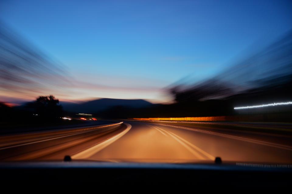 Blick aus dem fahrenden Auto auf eine Landstraße in der Dämmerung